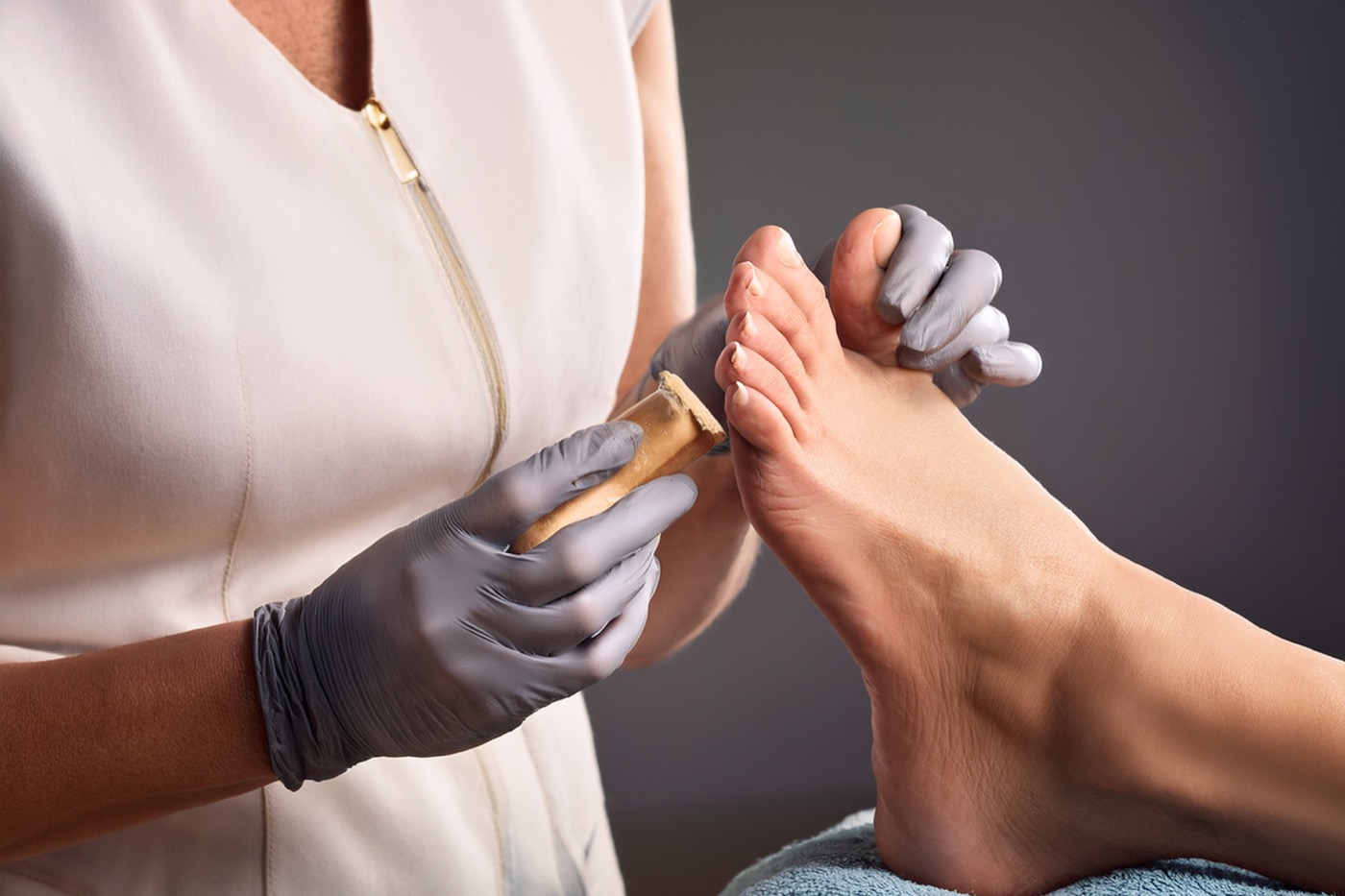 Behandlung eines Fußes durch eine Fußpflegerin mit Handschuhen